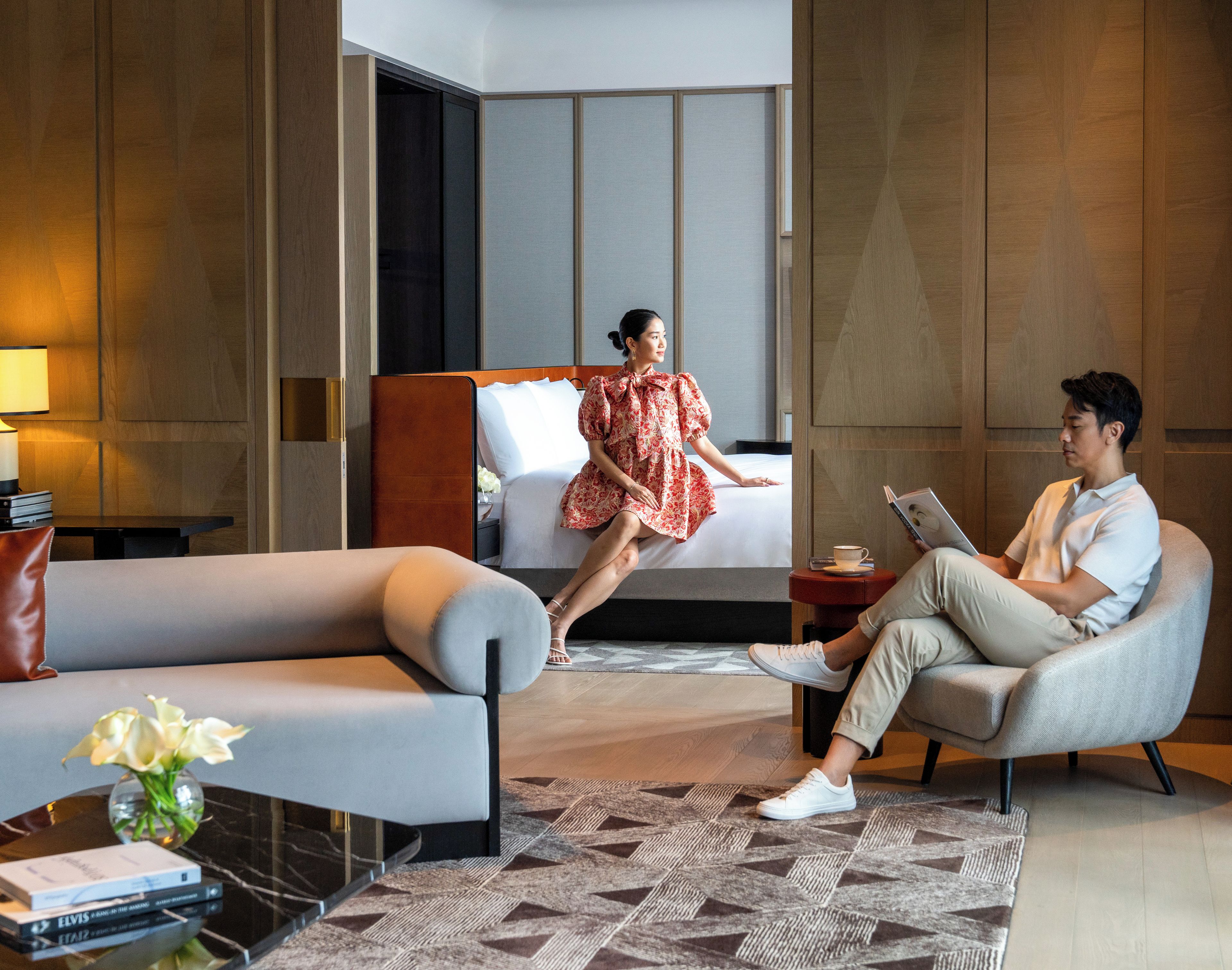 A hotel room with a bed, a sofa, a coffee table with books, and a small table with a cup and a book.
