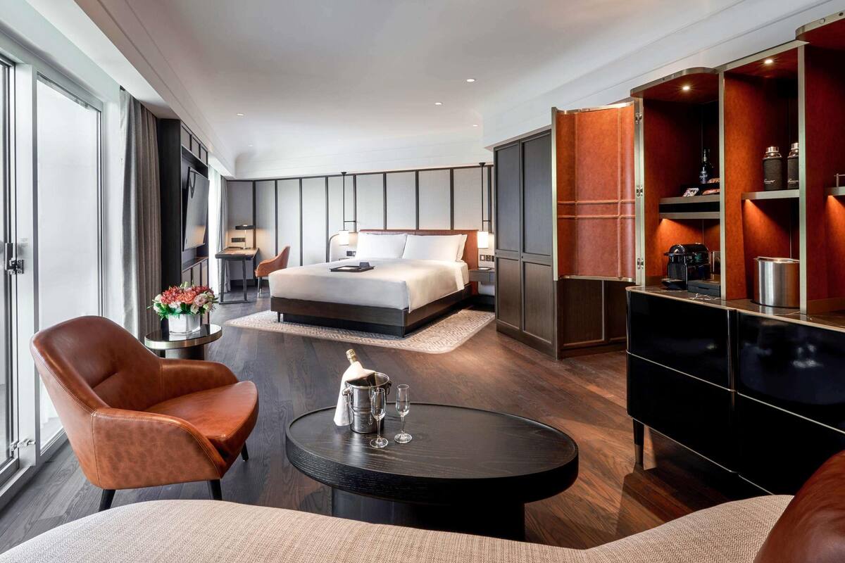 A modern hotel room with a large bed, a seating area with a coffee machine, and a view of the city.