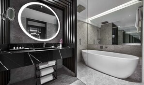 Een moderne badkamer met een vrijstaand bad, een grote spiegel met ronde lijst en een wastafelmeubel van donker hout.