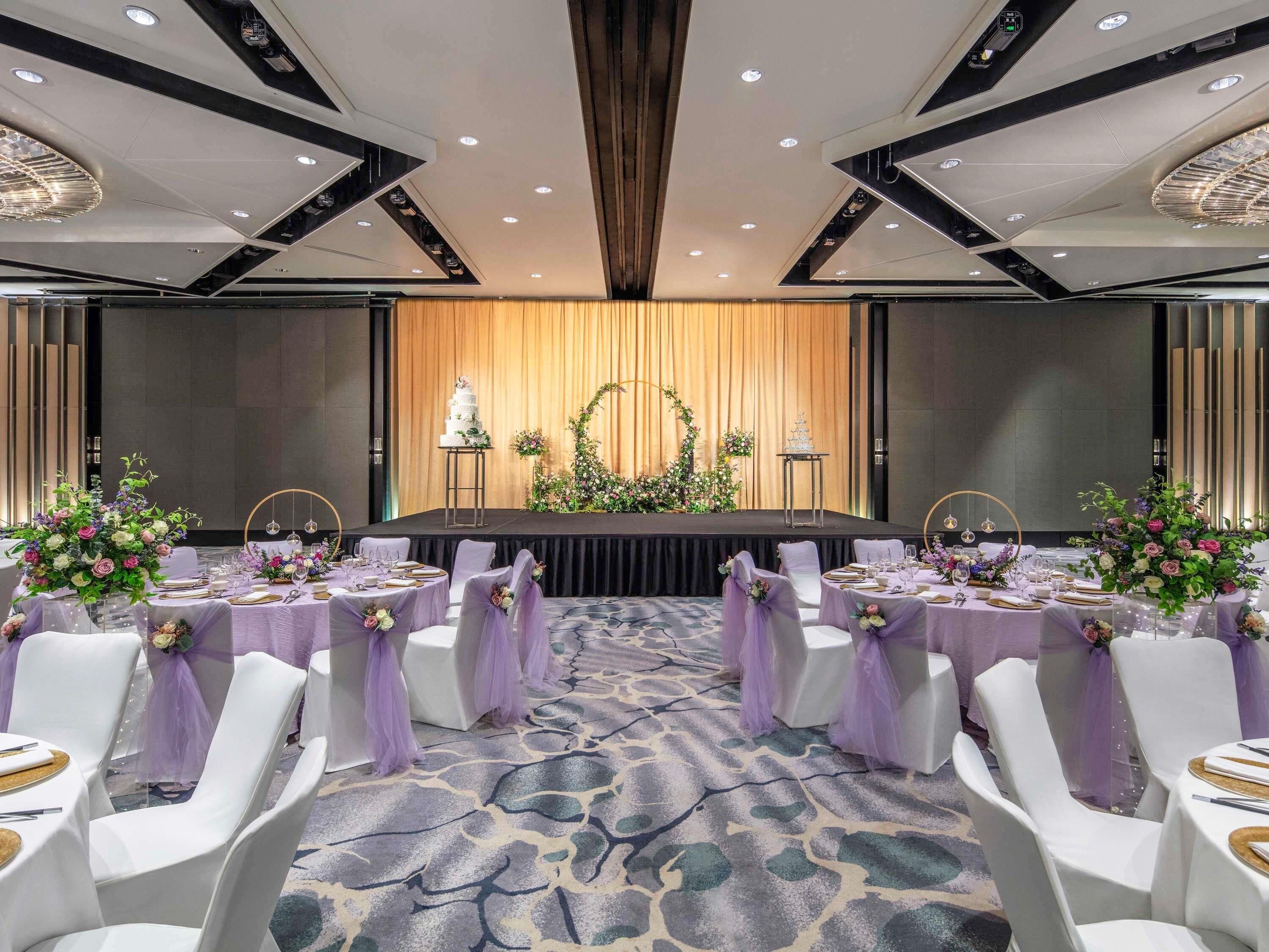 A banquet hall with round tables, white chairs, and purple sashes.