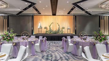 A banquet hall with round tables, white chairs, and purple sashes.