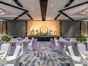 Un salón de banquetes con mesas redondas, sillas blancas y cintas moradas.