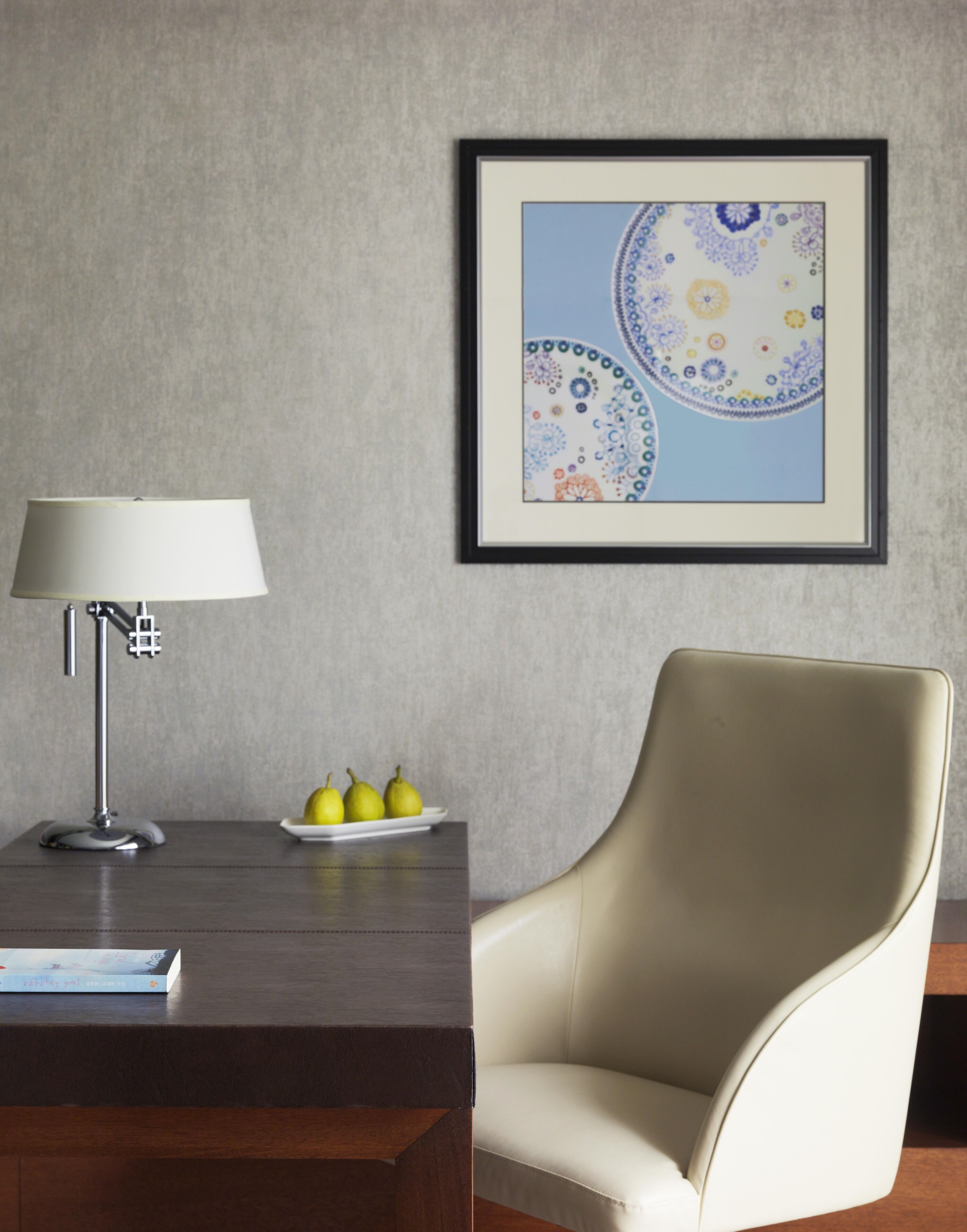 Een moderne kamer met een bureau, een lamp, een lijst met abstracte kunst en een stoel.