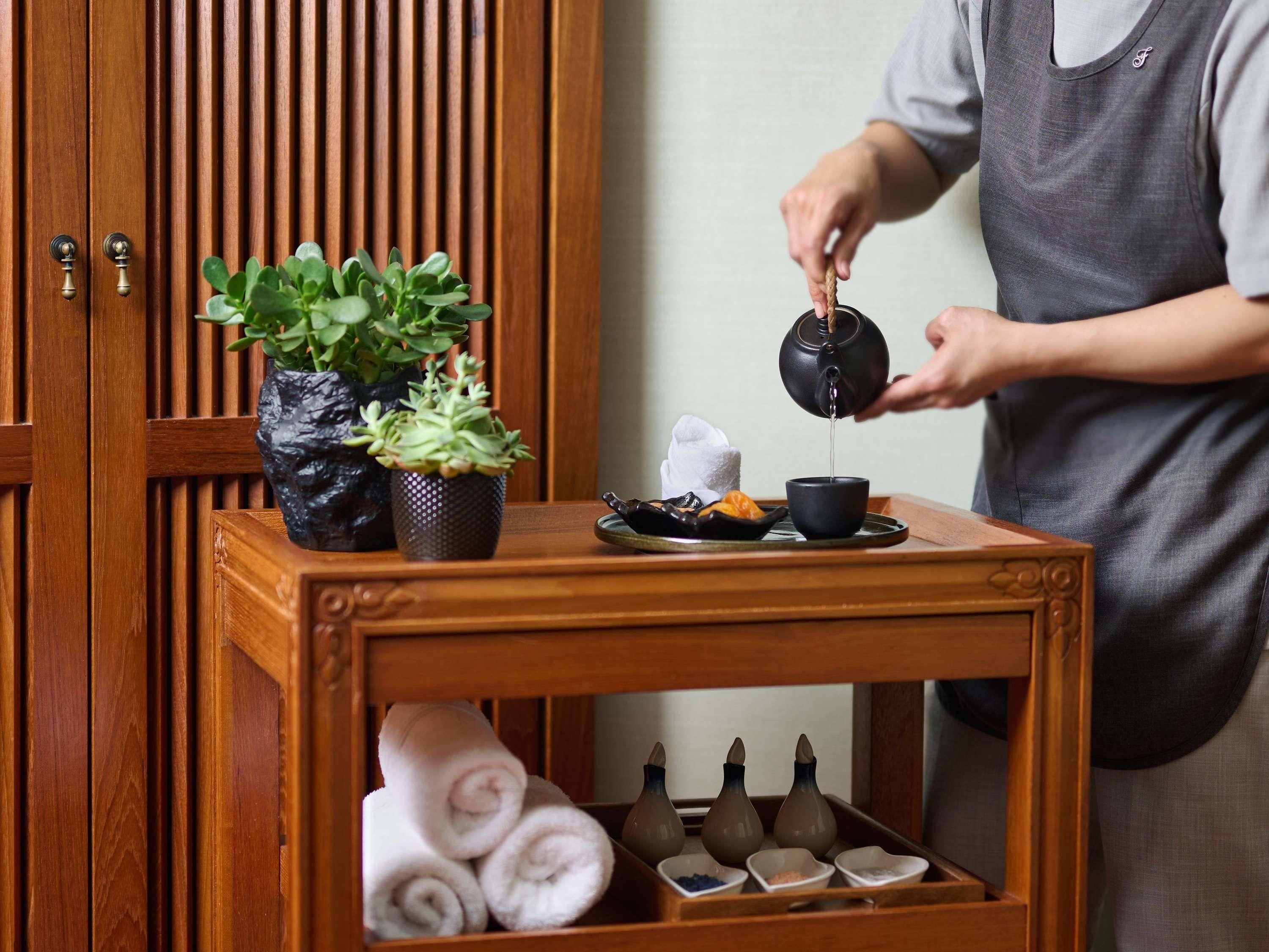 A wooden table with a tea set, including a teapot and cups, and a tray with towels and bottles.