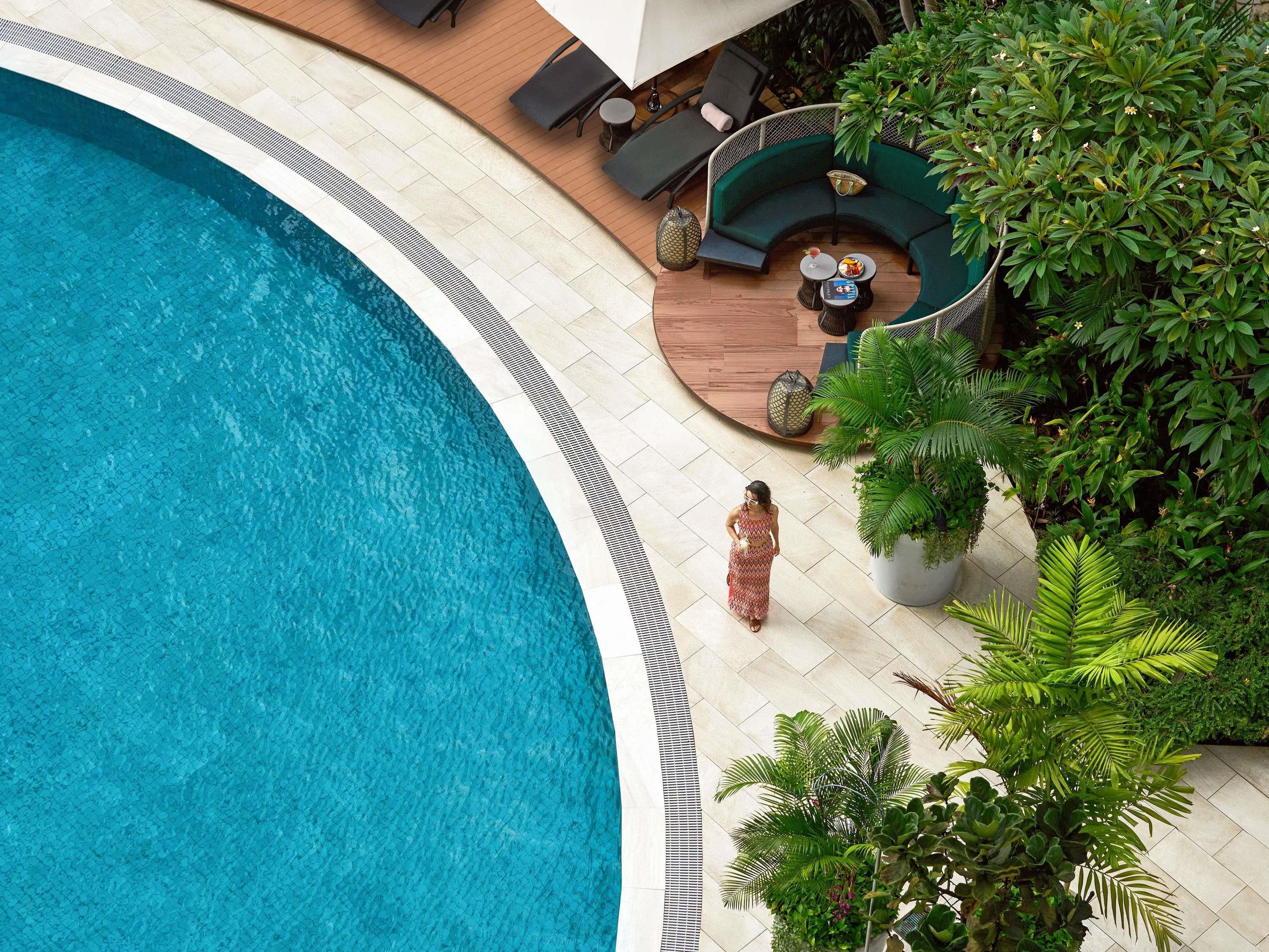 A poolside area with a curved pool, lounge chairs, a sofa, and potted plants.