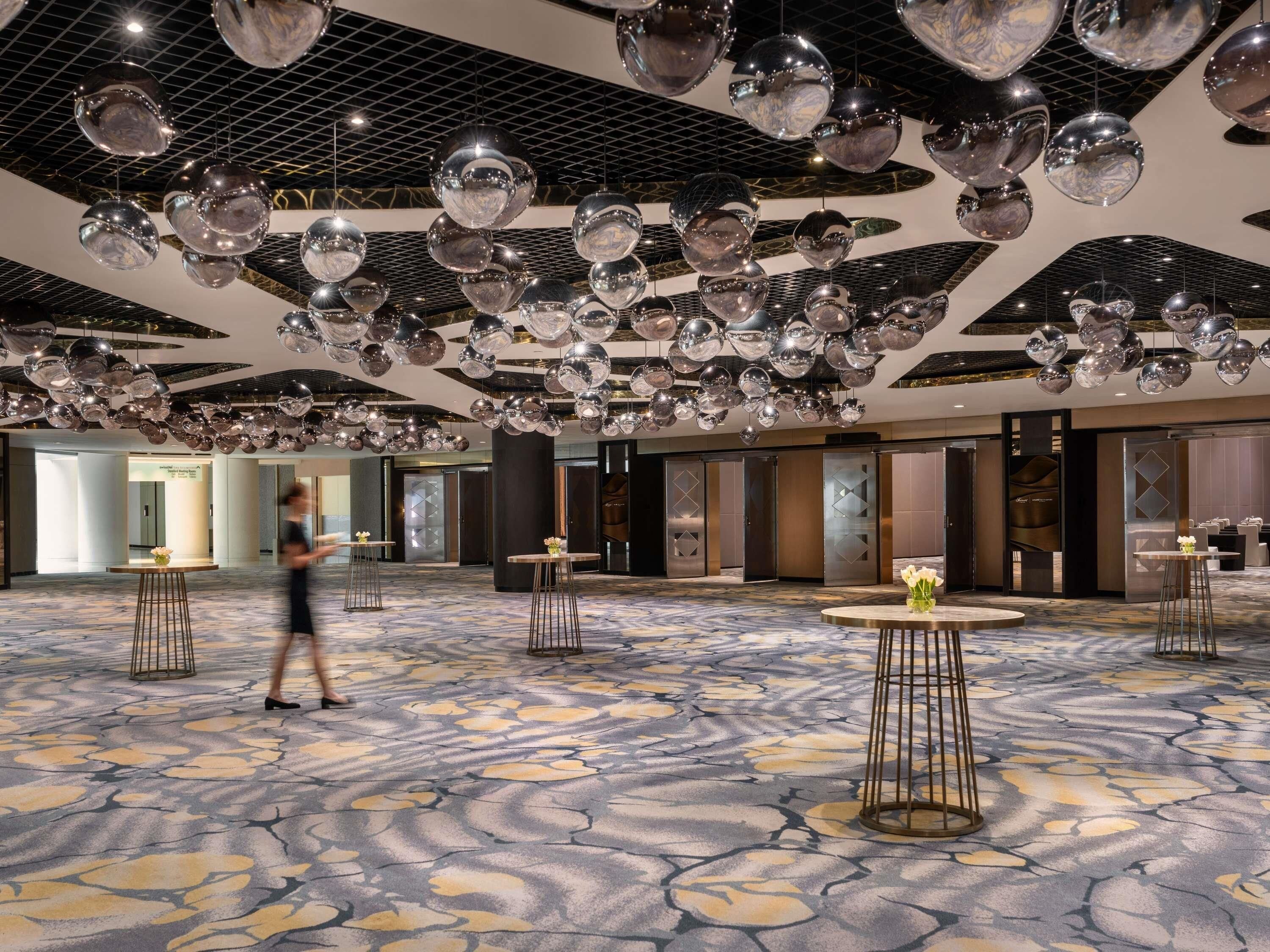 Un amplio vestíbulo de hotel con piso estampado, varias mesas redondas y un techo decorado con numerosas esferas.