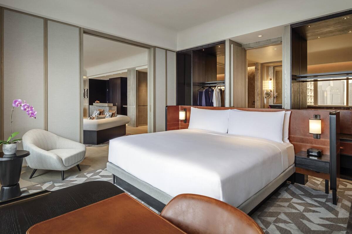 A modern hotel room with a large bed, a seating area, a vanity, and a mirror.