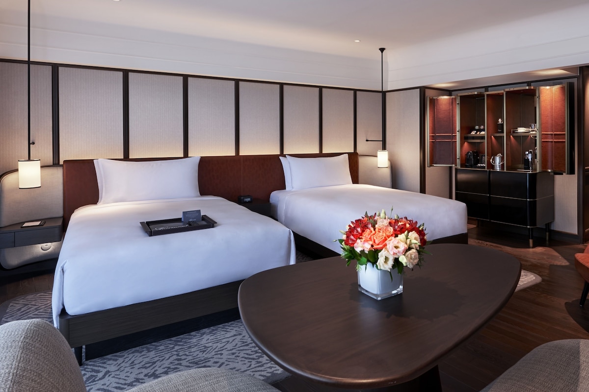 Een hotelkamer met twee bedden, een bureau, een stoel, een koffieapparaat en een minibar.