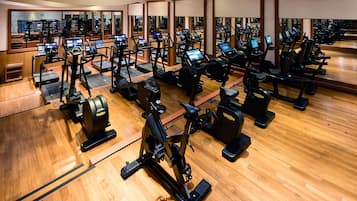 A gym with multiple exercise machines, wooden flooring, and mirrors reflecting the equipment.