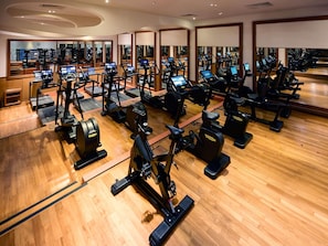 Un gimnasio con varias máquinas de ejercicio, suelo de madera y espejos que reflejan el equipamiento.