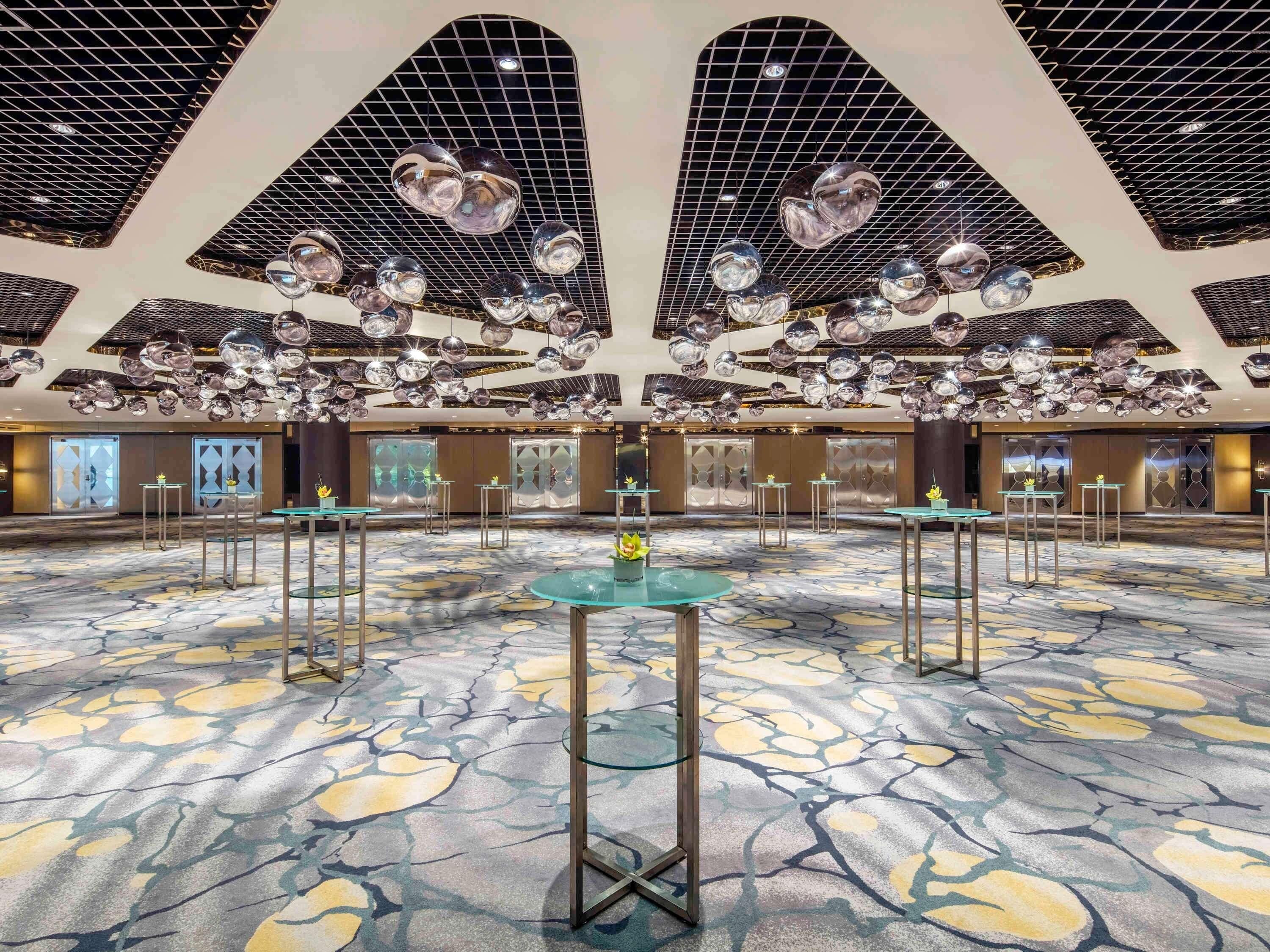 A spacious lobby with a patterned floor, multiple tables, and a ceiling with hanging spherical decorations.