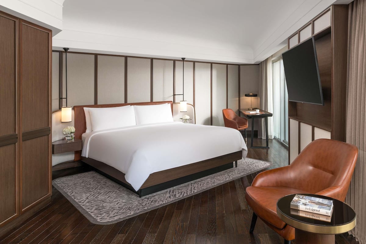 Une chambre d’hôtel avec un grand lit, un coin salon comprenant une chaise et une petite table, un téléviseur fixé au mur et un tapis à motifs.