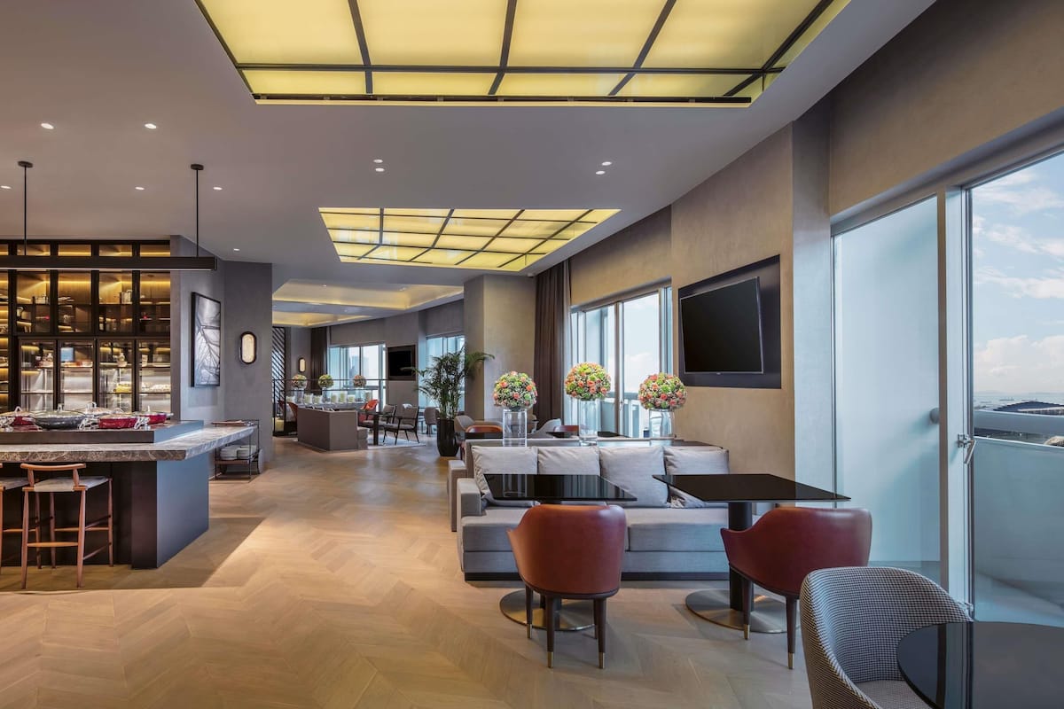 Un hall d’hôtel moderne doté d’un espace salon central, d’un bar et d’une grande fenêtre donnant sur la ville.