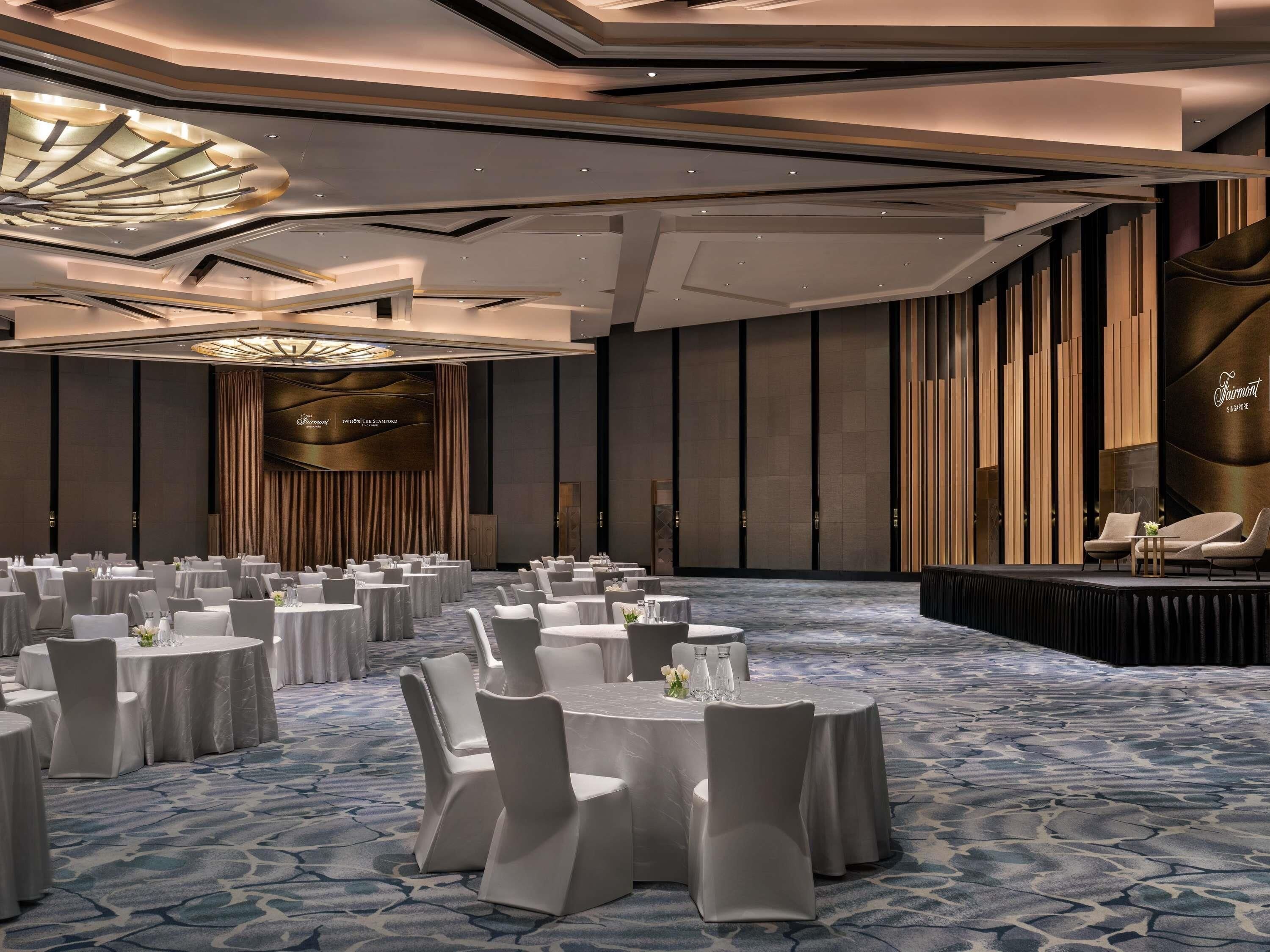 A conference room with round tables, white chairs, and a stage with seating.