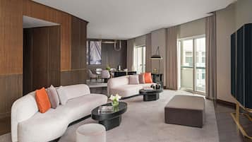 A modern hotel room with a sectional sofa, a round coffee table, a small side table, and a large window offering a view of the city.