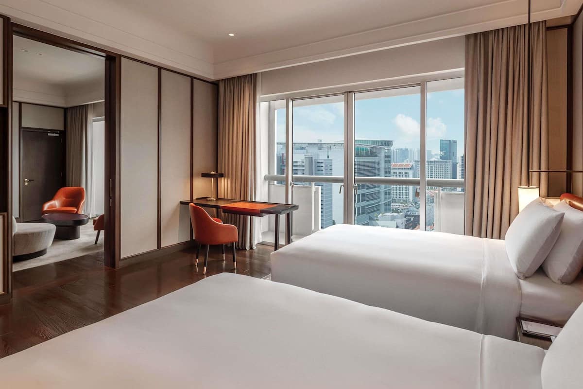 A hotel room with two beds, a desk, a chair, and a view of the cityscape.