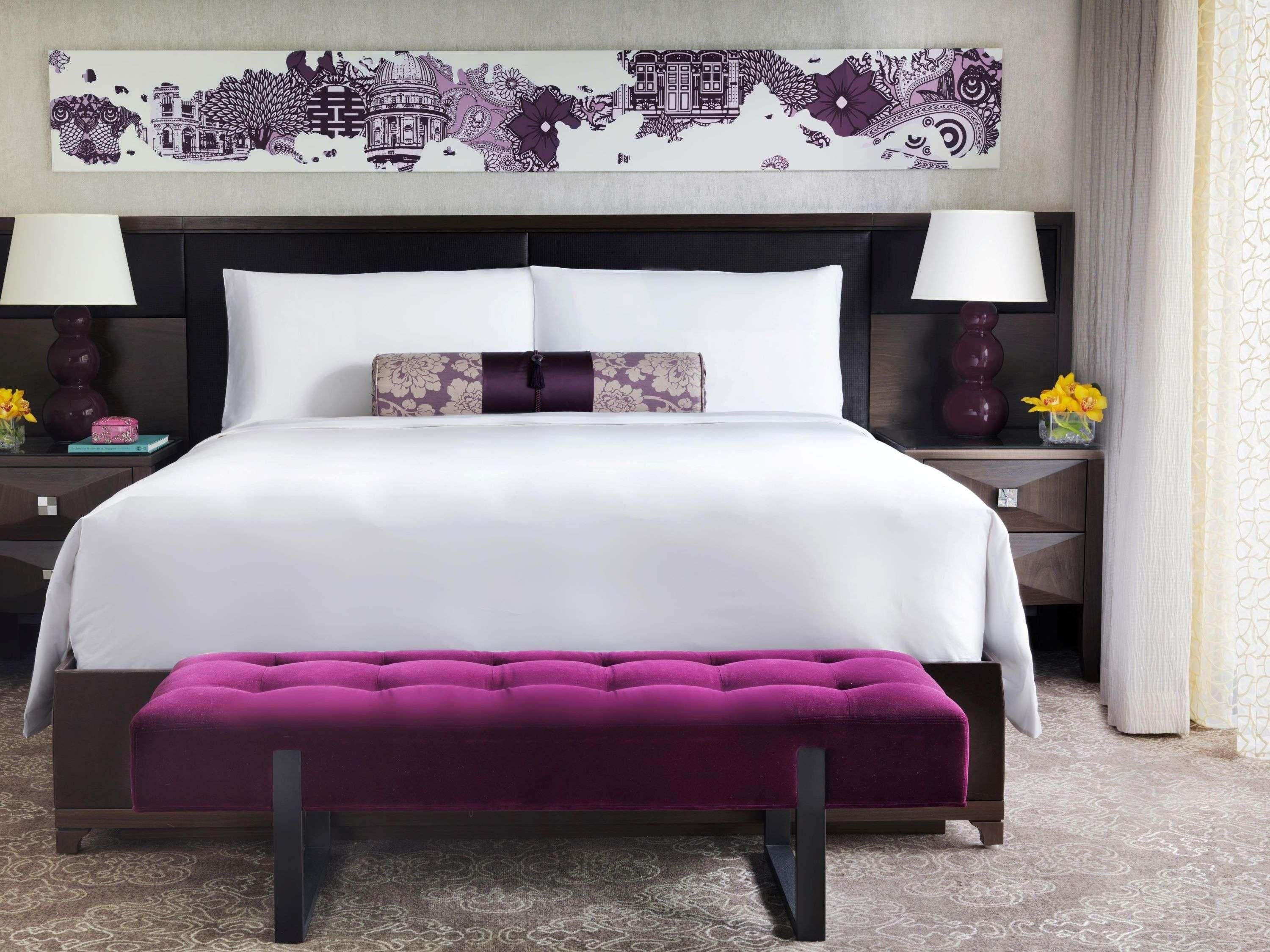 Ein Bett mit weißer Bettwäsche, eine violette Polsterbank und ein dekorativer Kopfteil.