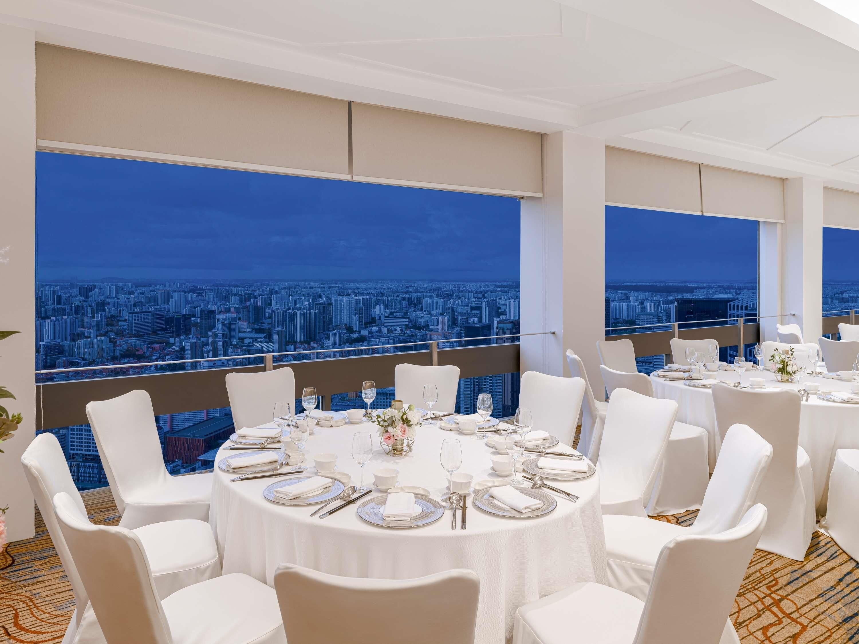 Un restaurante con mesas redondas dispuestas para comer, sillas blancas y vistas a la ciudad.