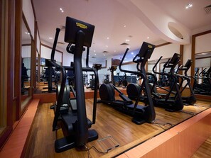 Un gimnasio con máquinas de cardio, espejos y suelo de madera.