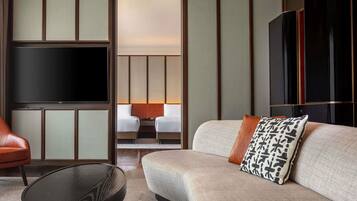 Una habitación de hotel moderna con un televisor de pantalla plana grande, un sofá con cojines estampados, un sillón de cuero y una mesa de centro redonda.