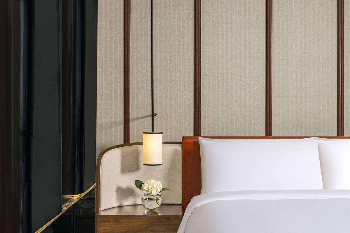 A hotel room with a bed, a nightstand, a lamp, and a vase with flowers.