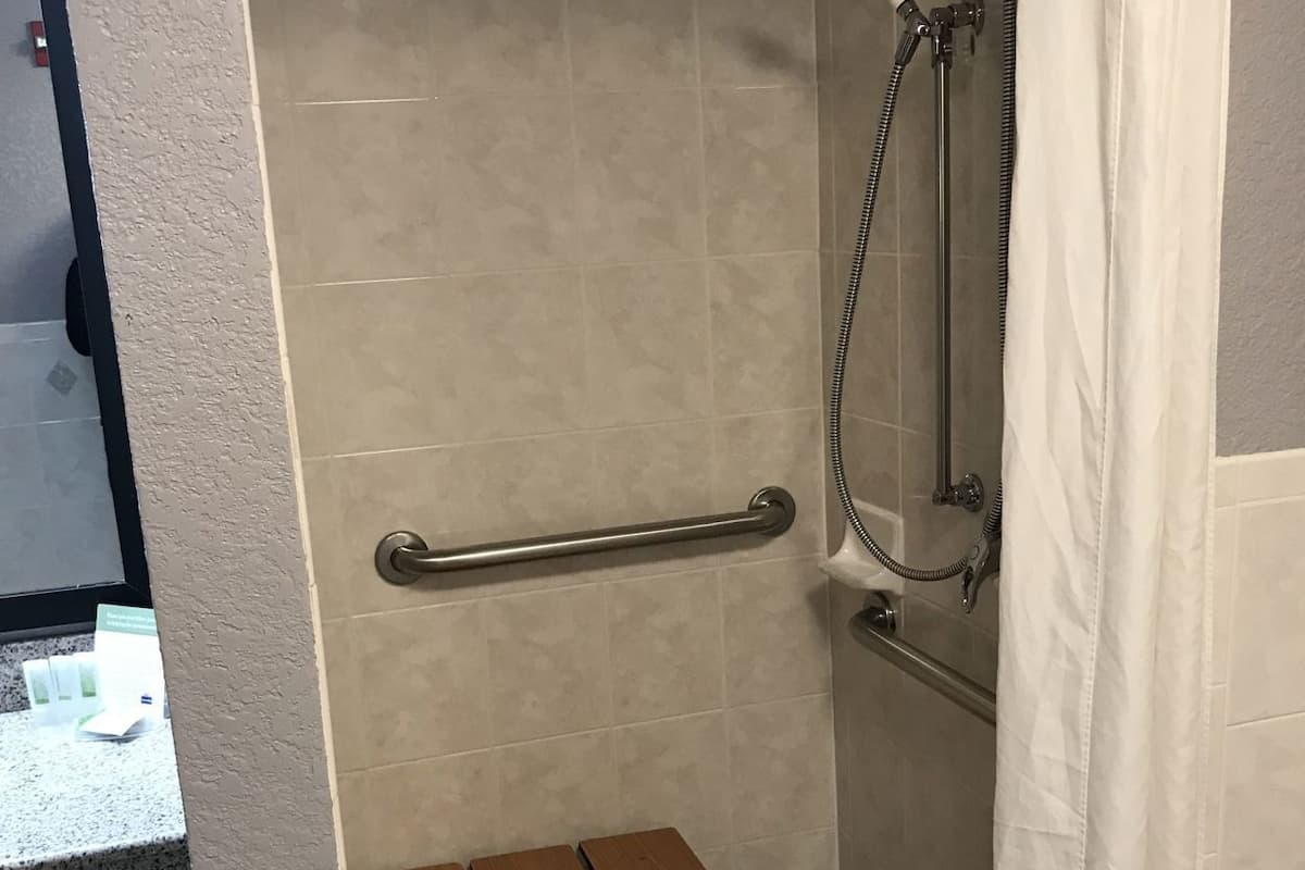A shower area with a grab bar, a bench, and a showerhead.