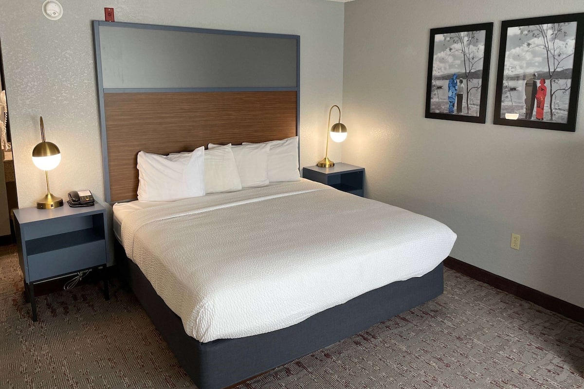 A hotel room with a large bed, two bedside tables with lamps, a headboard, and two framed pictures on the wall.