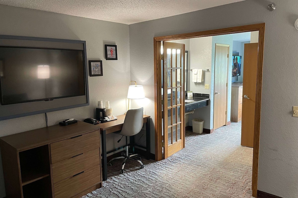 A hotel room with a desk, chair, TV, and a bathroom visible through an open door.