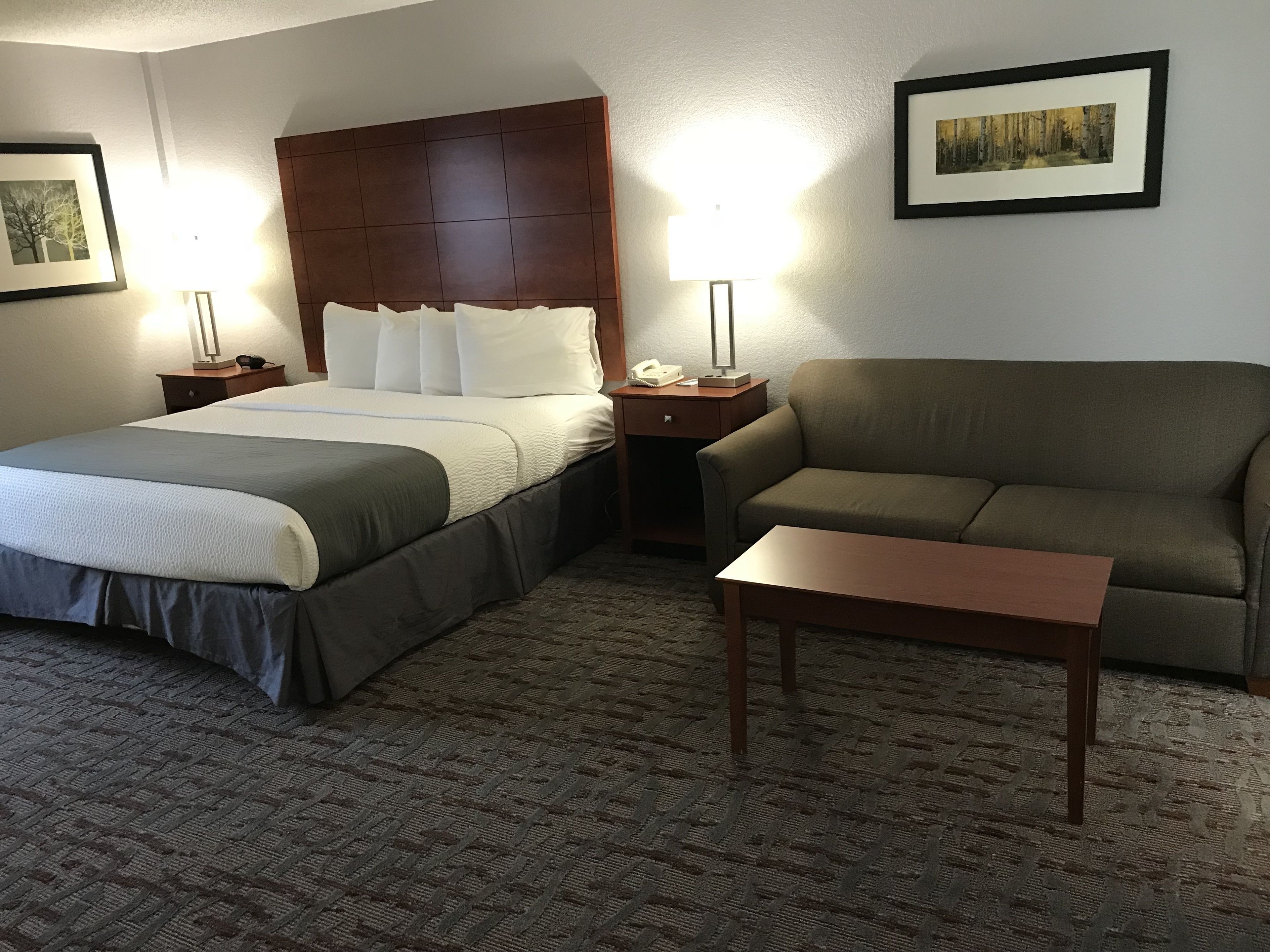 A hotel room with two beds, a sofa, a small table, and two bedside lamps.