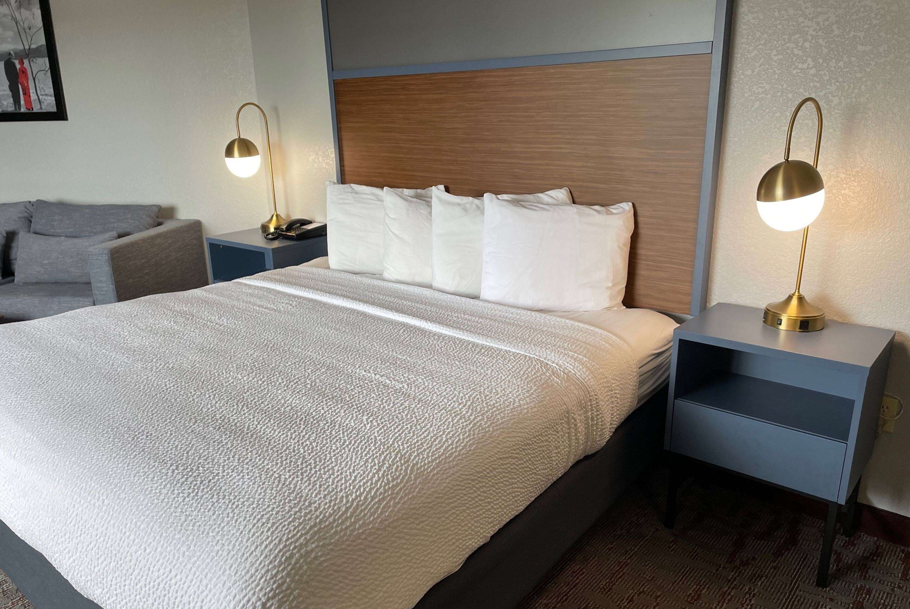 Una habitación de hotel con una cama grande, dos mesitas de noche, un tocador, una lámpara y un sofá.