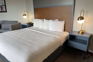 Una habitación de hotel con una cama grande, dos mesitas de noche, un tocador, una lámpara y un sofá.