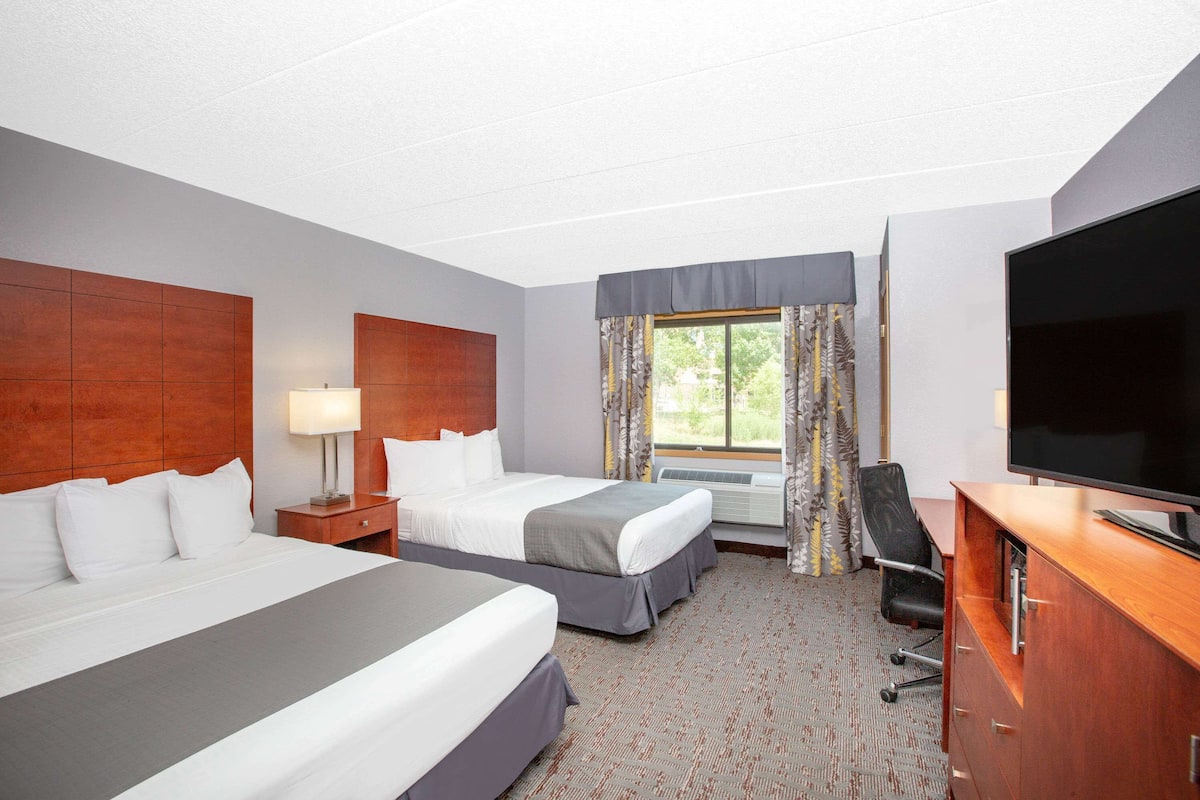 A hotel room with two beds, a desk, a chair, a TV, and a window with curtains.