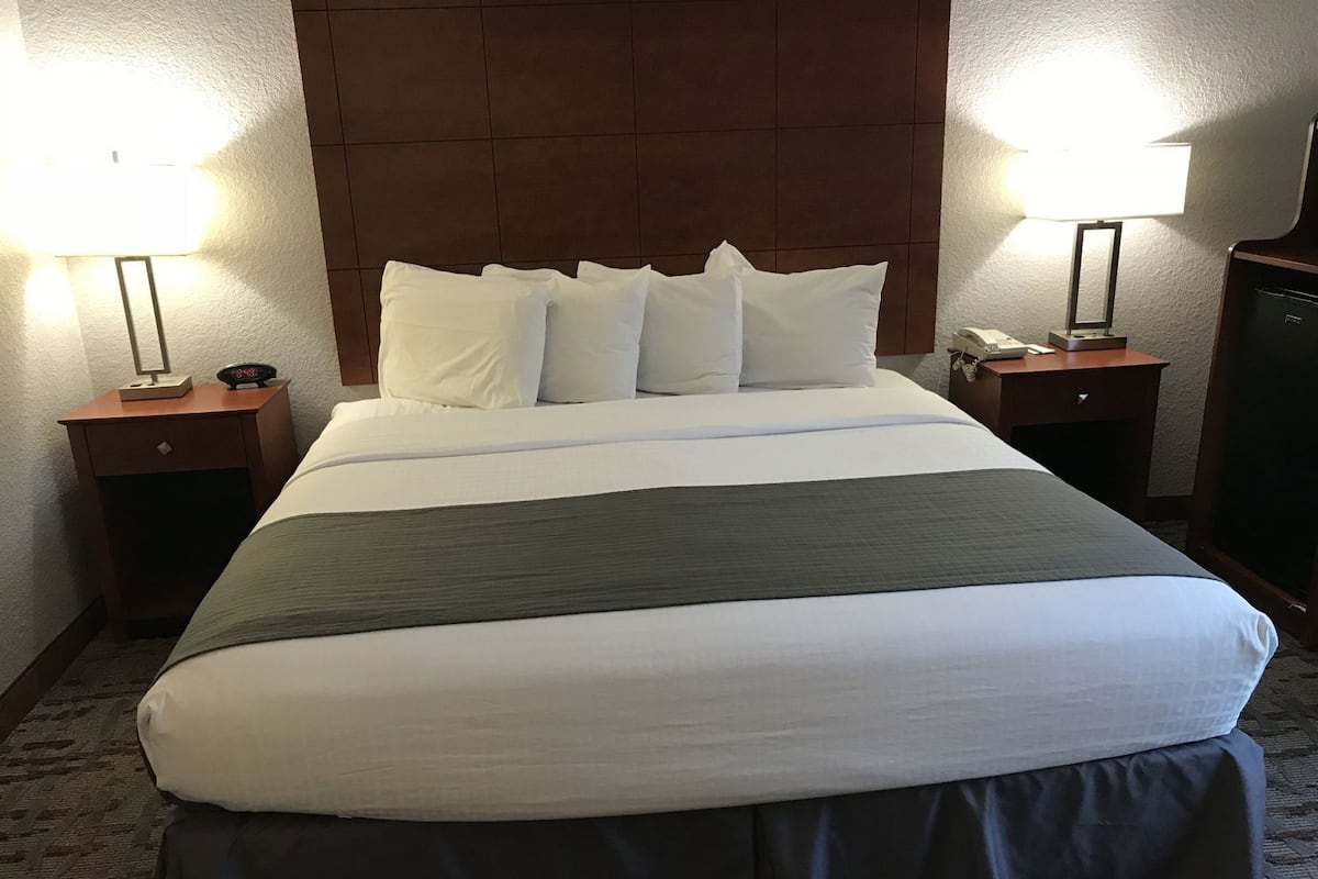 A hotel room with a large bed, two bedside tables, a nightstand, a desk, and a lamp.