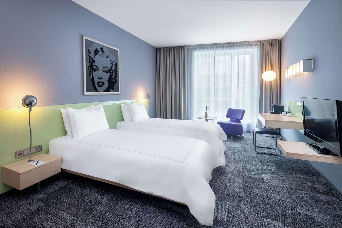 Een hotelkamer met twee bedden, een bureau, een televisie en een schilderij aan de muur.
