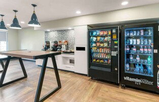 A modern kitchen with a dining table, two beverage vending machines, and a coffee machine.