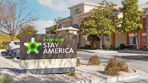 En skylt för hotellkedjan Extended Stay America, med en modern byggnad i bakgrunden.