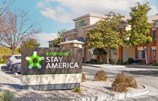 A sign for Extended Stay America with a modern building in the background.
