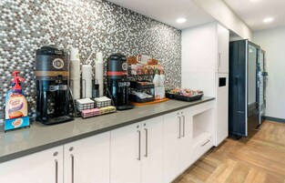 A modern kitchen with a coffee station, including a coffee machine, cups, and a coffee maker.