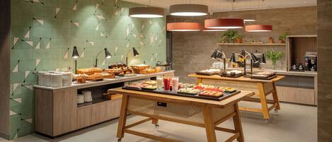 A modern breakfast buffet with various food items, a coffee station, and a seating area with a wooden table and chairs.