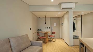 A modern, minimalist room with a sofa, a dining table with two chairs, a small kitchenette, and a walk-in closet.