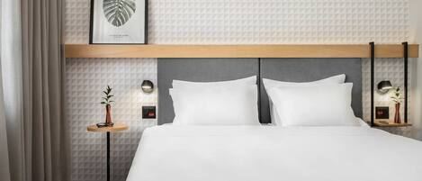 Ein Hotelzimmer mit einem großen Bett, einer gerahmten Blattform-Kunstwerk, zwei Nachttischen mit Lampen und einer Wand mit geometrischem Muster.