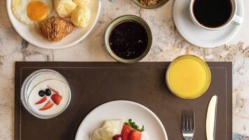 A breakfast setting with plates of food, a coffee cup, and a juice glass on a marble table.