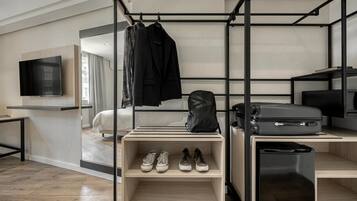 A modern hotel room with a bed, a TV, a desk with a computer, and a shoe rack.