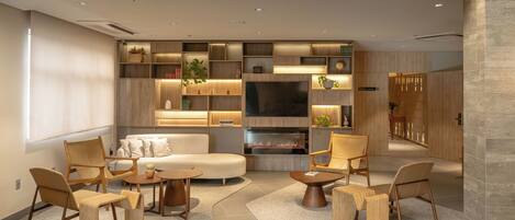 A modern living room with a sofa, chairs, a coffee table, and a TV. There are shelves with plants and decorative items.