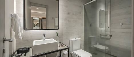 Un baño moderno con un espejo grande, un lavamanos blanco y una ducha con cerramiento de vidrio.