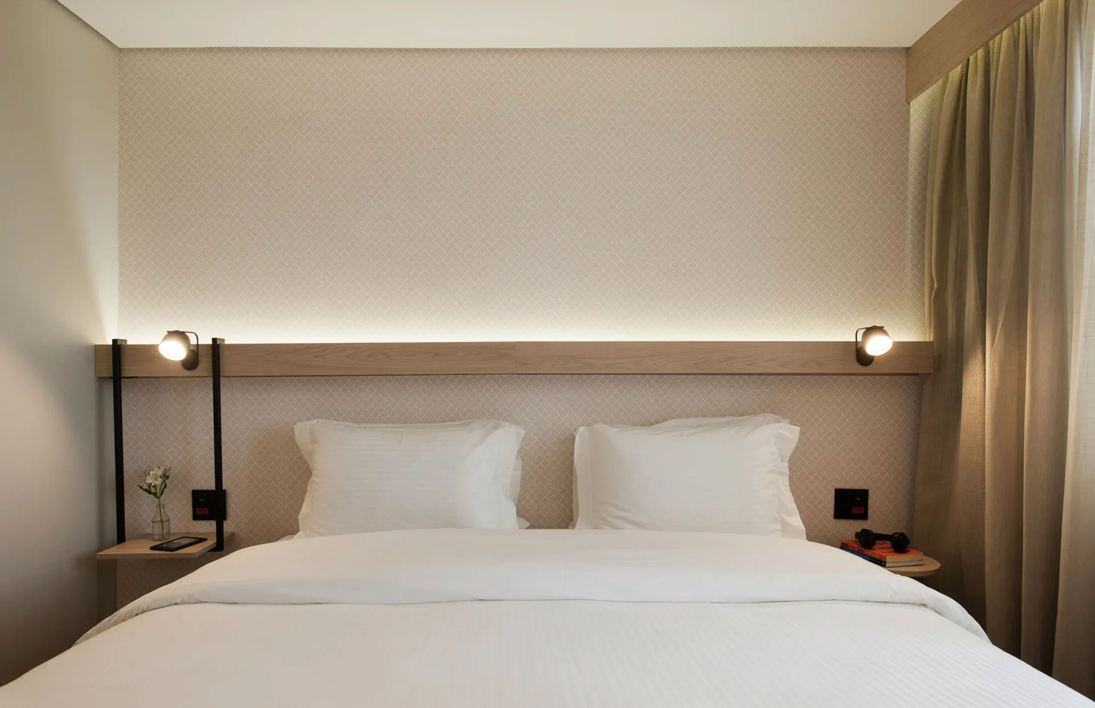 Habitación de hotel con una cama, dos mesitas de noche, una lámpara y un aplique de pared.