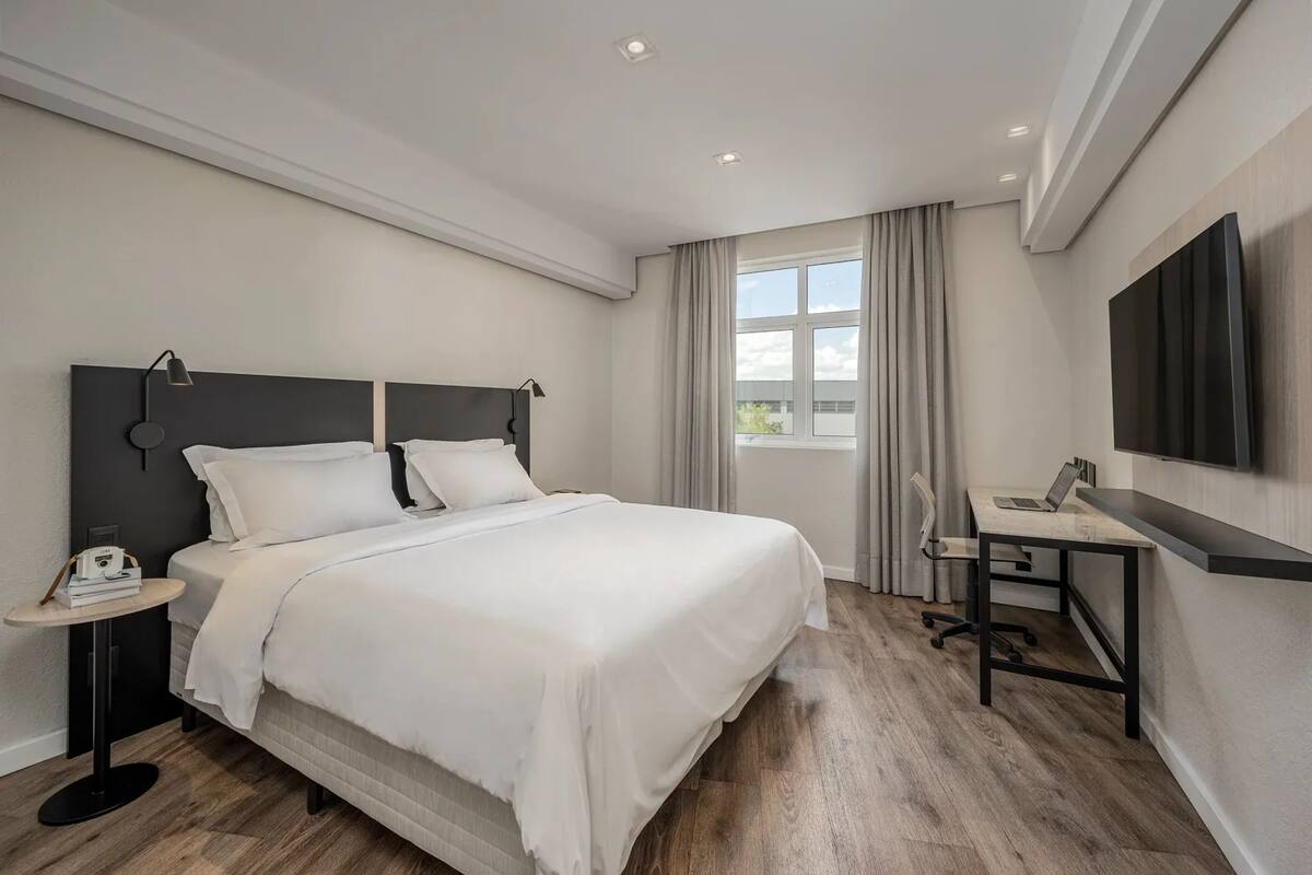 Ein modernes Hotelzimmer mit einem großen Bett, einem Schreibtisch, einem Stuhl und einem an der Wand befestigten Flachbildfernseher.