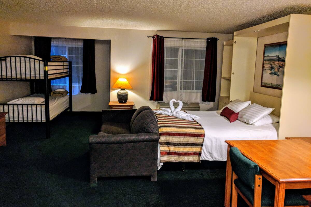 Ett hotellrum med en våningssäng, en enkelsäng, en soffa, ett bord och en lampa.