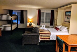 A hotel room with a bunk bed, a single bed, a sofa, a table, and a lamp.