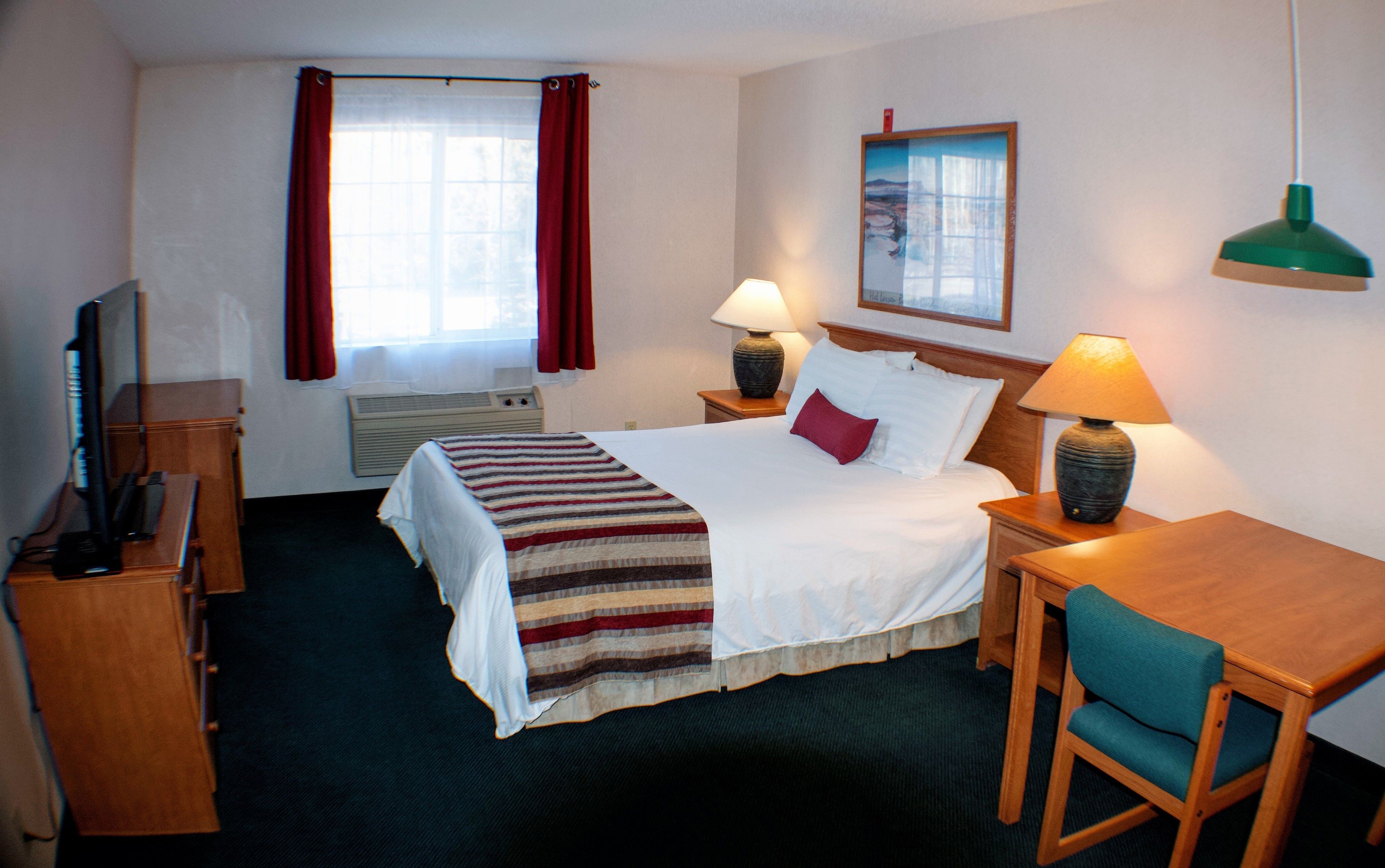 A hotel room with a bed, a desk, a chair, a TV, and a window with curtains.